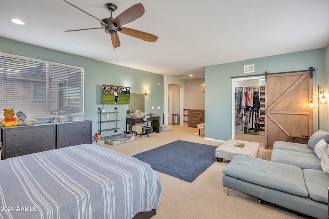 bedroom featuring ceiling fan, carpet flooring, a walk in closet, a closet, and a barn door