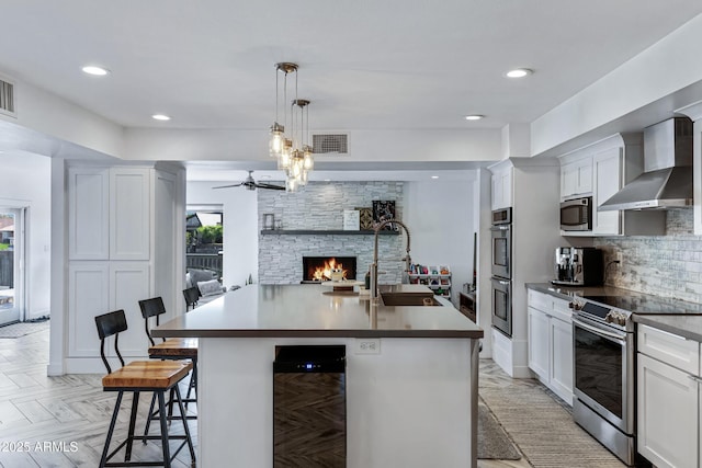 kitchen with visible vents, wall chimney exhaust hood, appliances with stainless steel finishes, a stone fireplace, and a sink