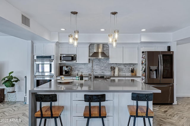 kitchen featuring visible vents, wall chimney exhaust hood, a kitchen breakfast bar, stainless steel appliances, and backsplash