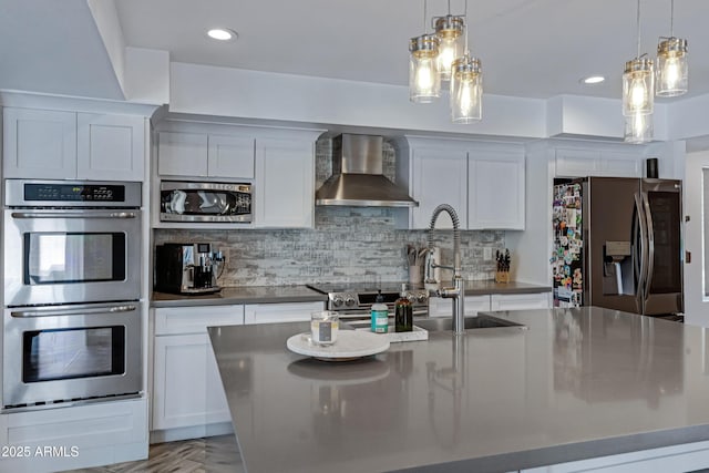 kitchen featuring a kitchen island with sink, stainless steel appliances, wall chimney range hood, backsplash, and decorative light fixtures