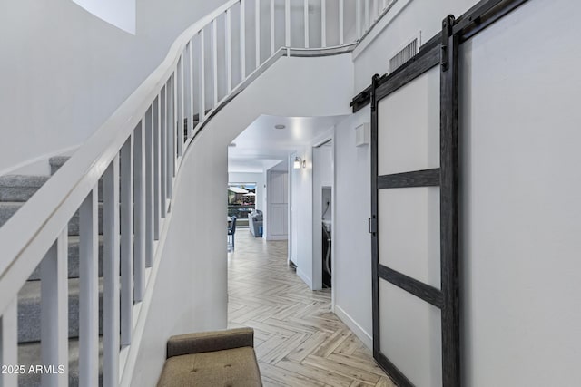 corridor featuring a towering ceiling, a barn door, and stairway