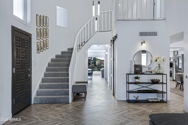 entrance foyer with a barn door, a towering ceiling, visible vents, a healthy amount of sunlight, and stairway