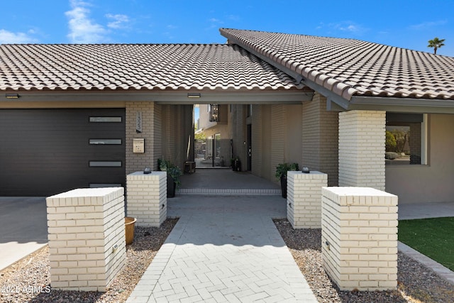 entrance to property with a tiled roof, brick siding, and driveway