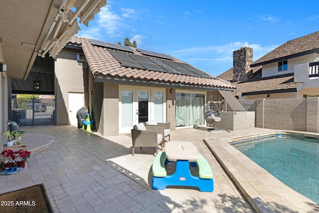 rear view of property featuring a tile roof, fence, a patio area, roof mounted solar panels, and stucco siding