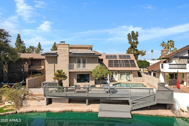 rear view of property with a balcony, solar panels, an outdoor pool, stucco siding, and a chimney