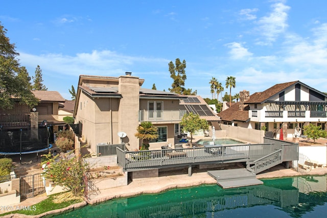 back of property featuring an outdoor pool, a balcony, a chimney, a trampoline, and roof mounted solar panels