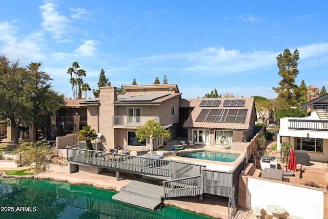 back of property featuring a patio, stucco siding, solar panels, a balcony, and an outdoor pool