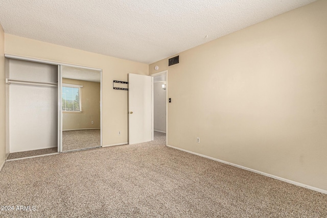 unfurnished bedroom with a textured ceiling, a closet, carpet flooring, and visible vents