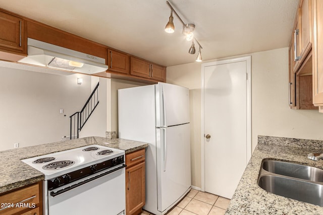 kitchen with white appliances, brown cabinets, under cabinet range hood, a sink, and light tile patterned flooring