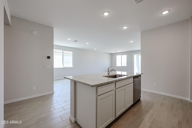 kitchen with light stone countertops, wood finish floors, dishwasher, a sink, and baseboards