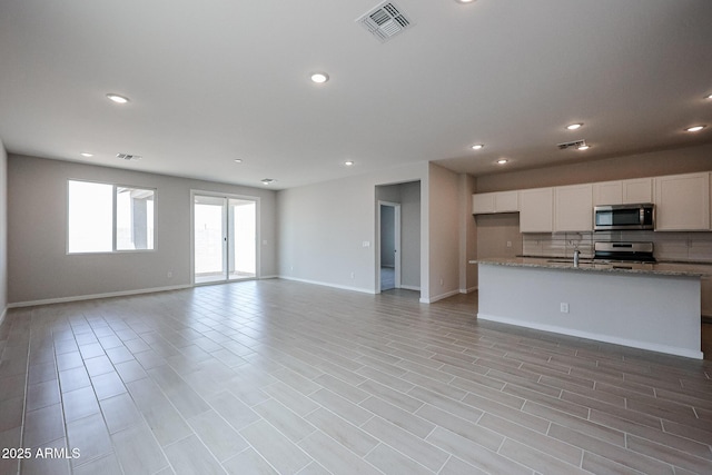 kitchen featuring visible vents, open floor plan, white cabinetry, appliances with stainless steel finishes, and backsplash