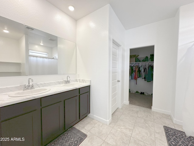 bathroom with double vanity, a sink, visible vents, and a walk in closet