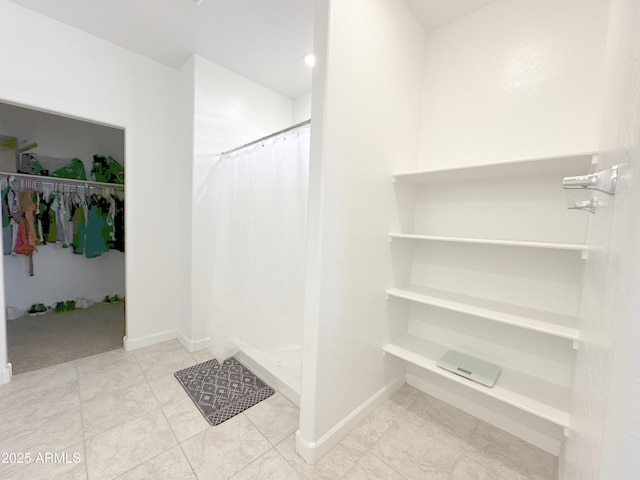 full bathroom featuring a shower stall, baseboards, and a walk in closet