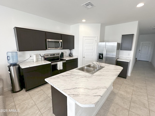 kitchen featuring a sink, visible vents, light countertops, appliances with stainless steel finishes, and a center island with sink