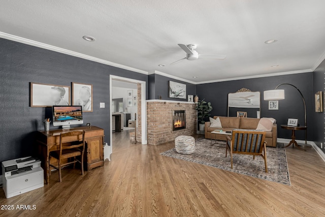 living room featuring wood finished floors, a brick fireplace, baseboards, ceiling fan, and ornamental molding