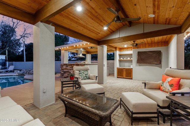 patio terrace at dusk featuring fence, an outdoor living space, a fenced in pool, a ceiling fan, and an outdoor kitchen