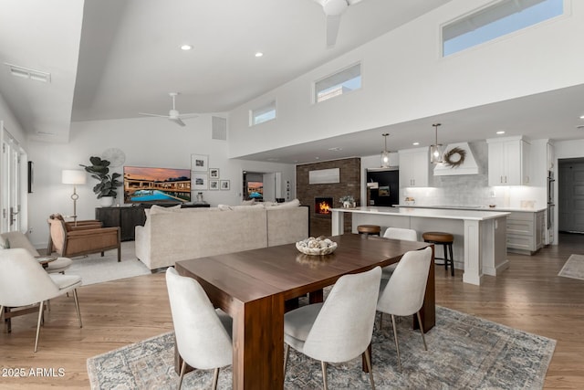 dining area featuring a ceiling fan, a brick fireplace, light wood-style flooring, and visible vents