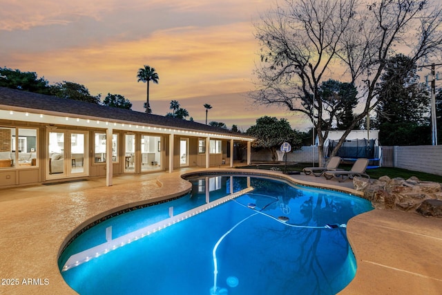 pool at dusk featuring a patio, fence, a trampoline, and a fenced in pool