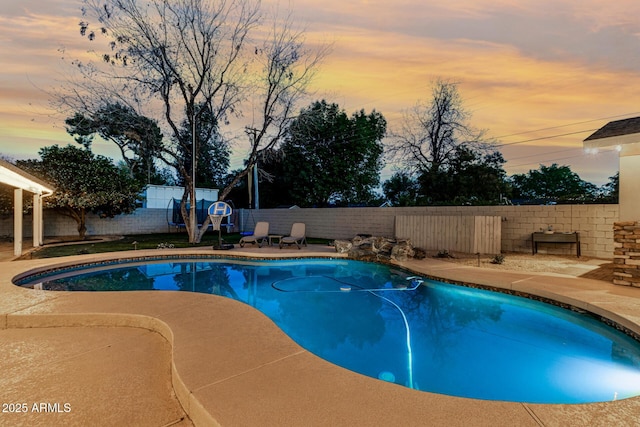 pool at dusk featuring a fenced backyard, a fenced in pool, and a patio