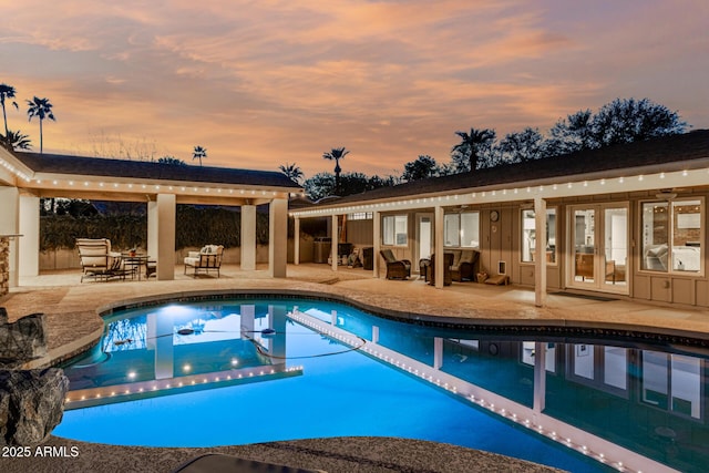 pool at dusk with an outdoor pool, french doors, and a patio area