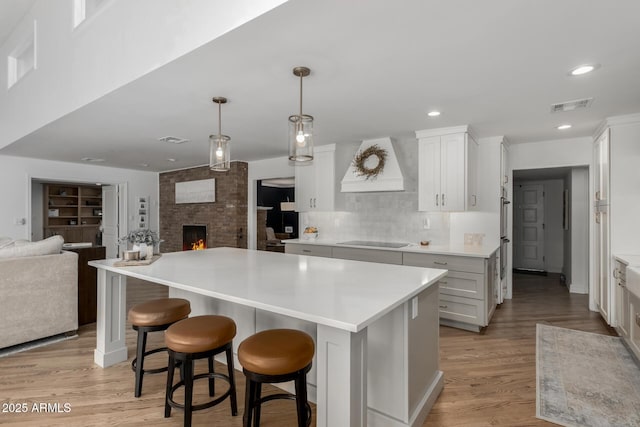 kitchen featuring black electric stovetop, open floor plan, visible vents, and premium range hood