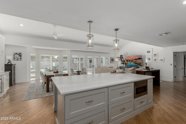 kitchen with light countertops, visible vents, light wood finished floors, stainless steel microwave, and gray cabinetry