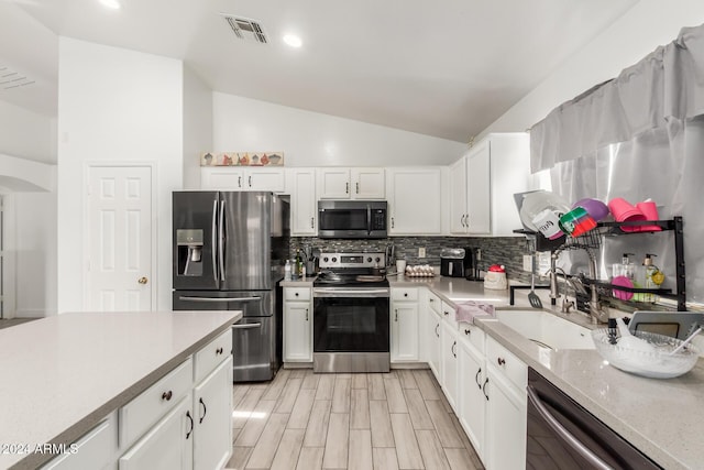 kitchen with white cabinets, sink, lofted ceiling, and stainless steel appliances