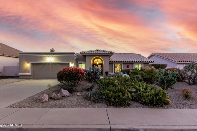 mediterranean / spanish-style house featuring a garage, driveway, a tiled roof, and stucco siding