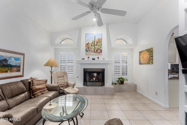 living area featuring light tile patterned floors, ceiling fan, high vaulted ceiling, a tile fireplace, and baseboards