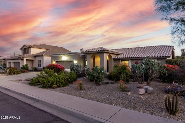 mediterranean / spanish home with a garage, a tile roof, and stucco siding