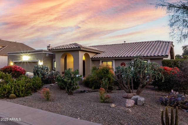 mediterranean / spanish house featuring a garage, a tiled roof, and stucco siding