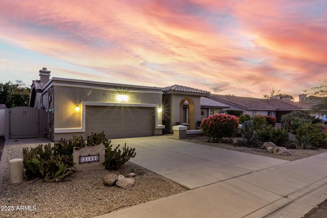 view of front of property with an attached garage, a tile roof, driveway, a gate, and stucco siding