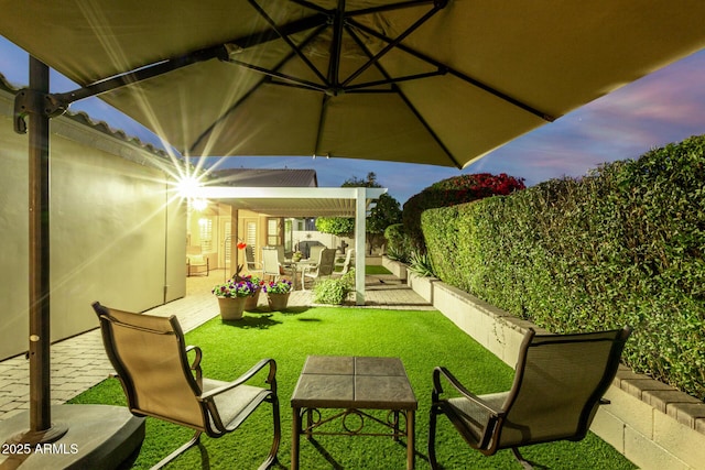 patio terrace at dusk featuring a fenced backyard and a yard