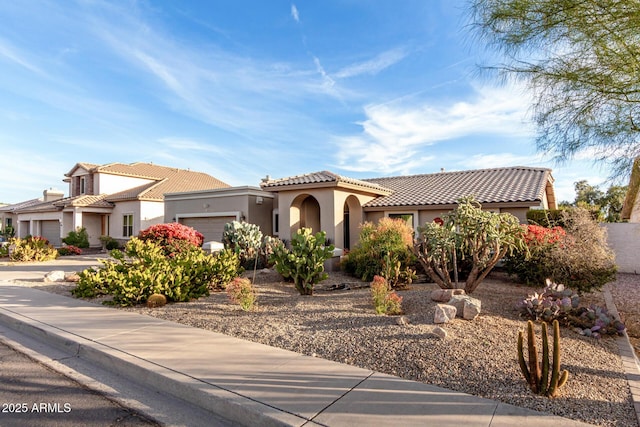 mediterranean / spanish-style house with an attached garage, a tile roof, and stucco siding