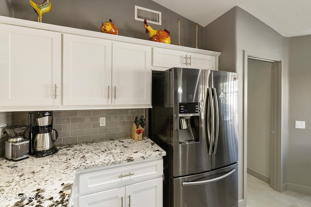 kitchen featuring white cabinets, lofted ceiling, backsplash, stainless steel fridge with ice dispenser, and light stone counters