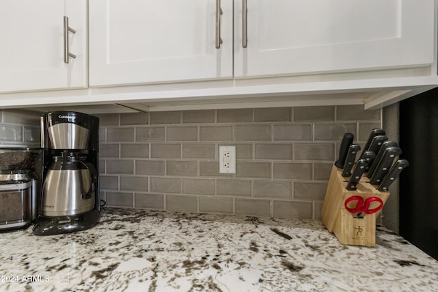 details with decorative backsplash, light stone counters, and white cabinetry