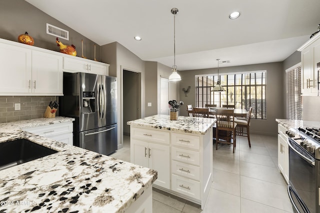 kitchen featuring appliances with stainless steel finishes, lofted ceiling, a kitchen island, pendant lighting, and light stone counters