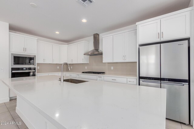 kitchen with white cabinetry, stainless steel appliances, sink, wall chimney exhaust hood, and a center island with sink