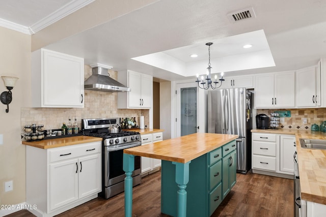 kitchen featuring stainless steel appliances, white cabinets, butcher block countertops, and wall chimney exhaust hood