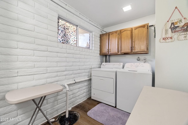 washroom featuring dark wood-type flooring, cabinets, brick wall, and washer and clothes dryer