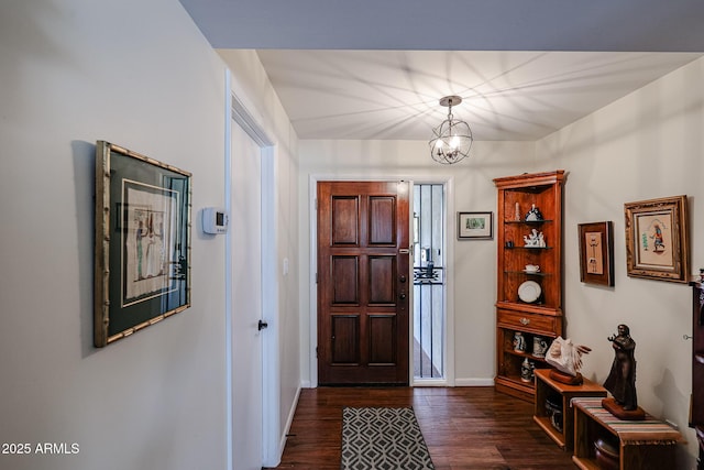 foyer entrance with dark wood-style floors, a notable chandelier, and baseboards