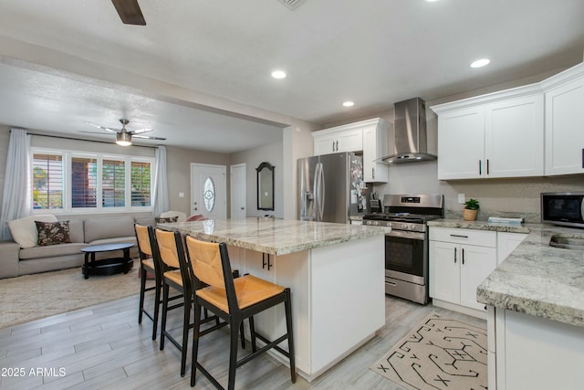 kitchen with a kitchen island, open floor plan, a kitchen bar, appliances with stainless steel finishes, and wall chimney exhaust hood