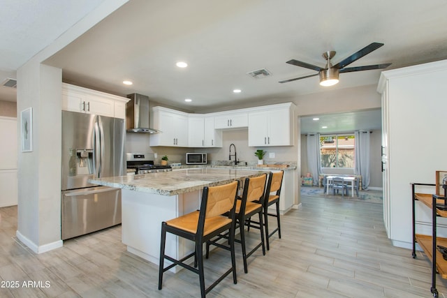 kitchen featuring visible vents, appliances with stainless steel finishes, white cabinets, wall chimney exhaust hood, and a sink