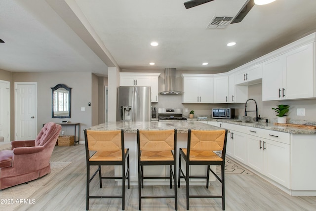 kitchen with stainless steel appliances, visible vents, ceiling fan, and wall chimney range hood