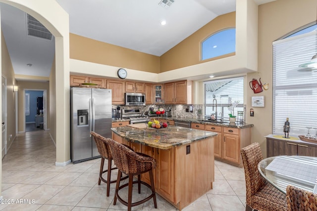 kitchen featuring a sink, stainless steel appliances, dark stone counters, light tile patterned flooring, and a center island