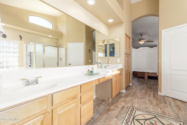 bathroom with double vanity, wood finished floors, a sink, a shower stall, and ceiling fan