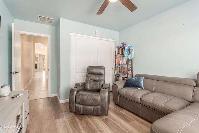living room with visible vents, light wood-style flooring, arched walkways, a ceiling fan, and baseboards