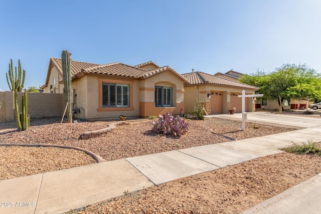mediterranean / spanish home featuring driveway, a tiled roof, fence, a garage, and stucco siding