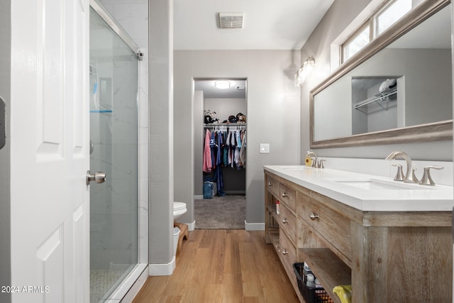 bathroom featuring wood-type flooring, toilet, vanity, and a shower with shower door