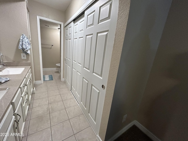 full bath with a textured wall, a sink, double vanity, toilet, and tile patterned floors